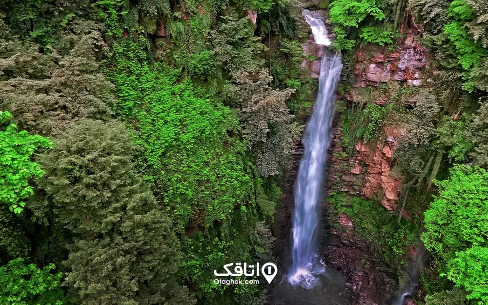 آبشاری بلند در خال جاری شدن از روی سنگ هایی خزه بسته در جنگل