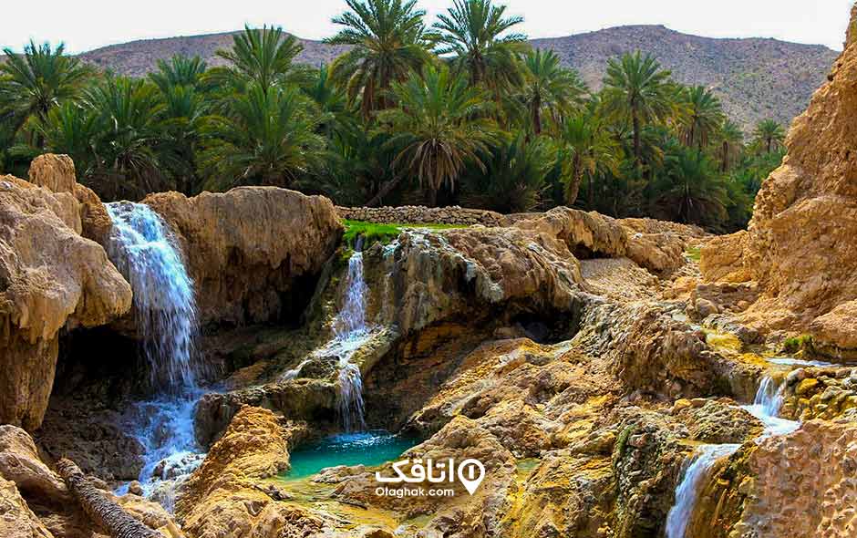 صخره هایی که از روی آنها آب جاری است و تعداد زیادی نخل که در اطراف این صخره ها وجود دارد