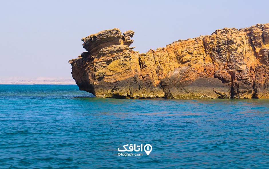یک صخره جلو امده در دریا و دریا آبی و آسمان صاف
