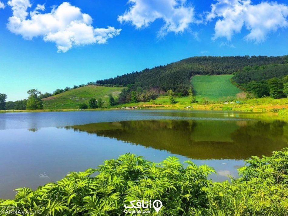 دریاچه ای در کنار تپه ای سر سبز و آسمانی آبی