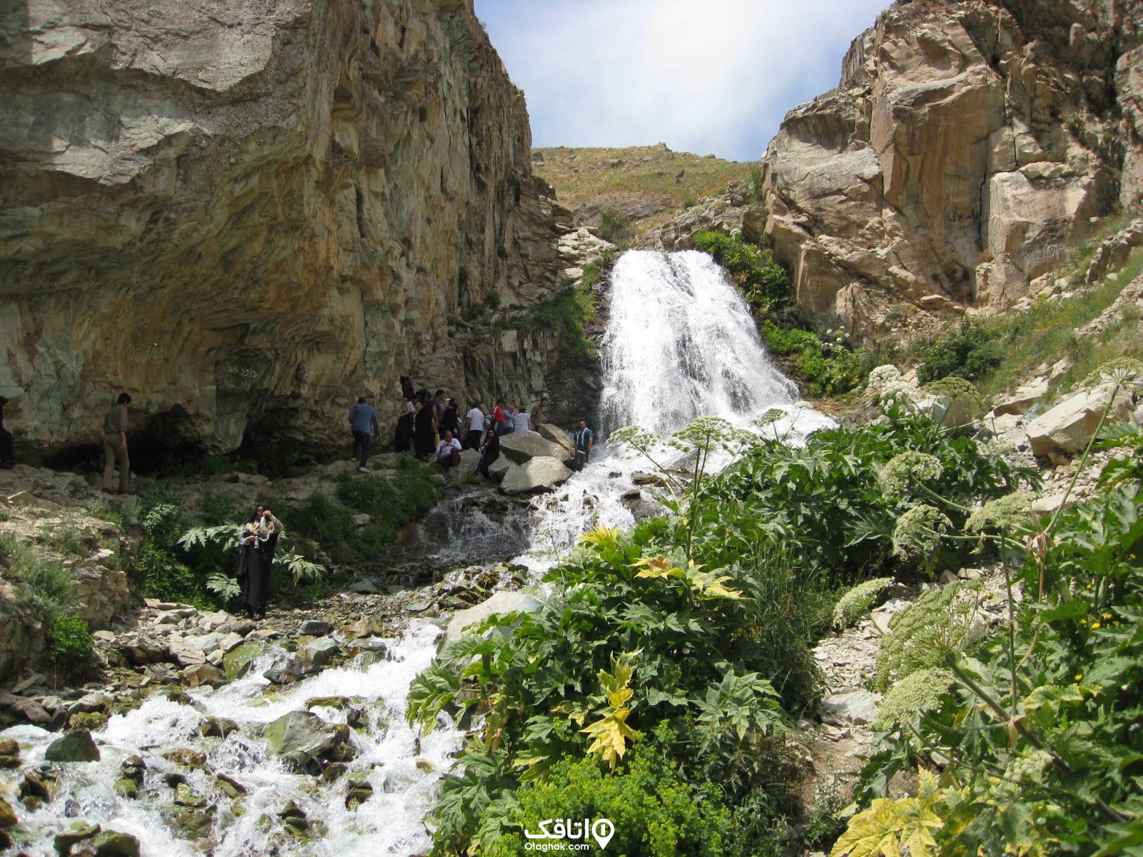 آبشاری در میان کوهستان و افرادی در حال بازدید از آن