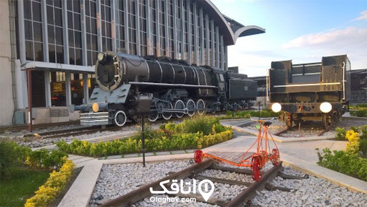 ساختمان راه آهن مشهد و یک لوکوموتیور قدیمی نمادین جلوی آن در محوطه گلکاری شده