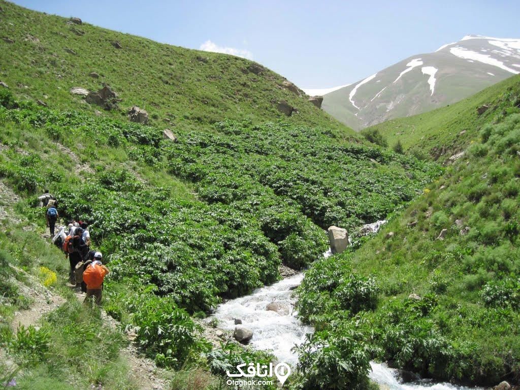 دشتی در میان سر سبز که در آن رودی جاری است و افرادی در حال گذر از آن 