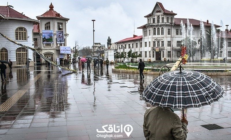 میدان شهرداری رشت در هوای بارانی و افرادی که چتر دارند