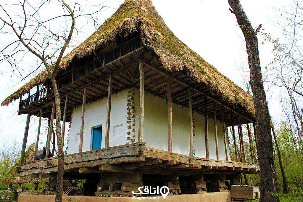کلبه چوبی با دیوارهای سفید رنگ و در آبی و سقفی که روی آن با کاه پر شده 