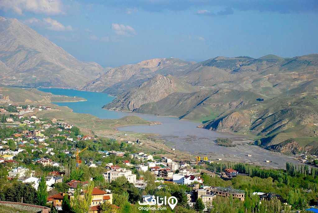 روستایی کنار یک رود با سقف های شبروانی رنگی و درختان سبز و در طرف دیگر رود کوه هایی هستند.