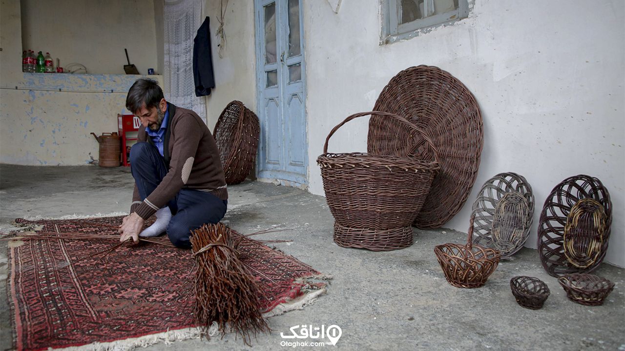 مردی در حال سبد بافی و چند سبد و اقلام حصیری در کنار دیوار