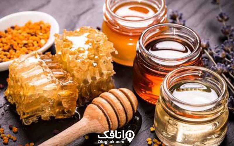 سه شیشه پر از عسل در کنار موم عسل و قاشق عسل خوری