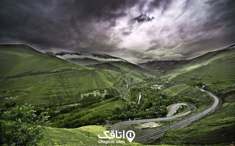 جاده ای پر و پیچ و خم در میان کوهستان سبز رنگ و آسمان آبری تیره