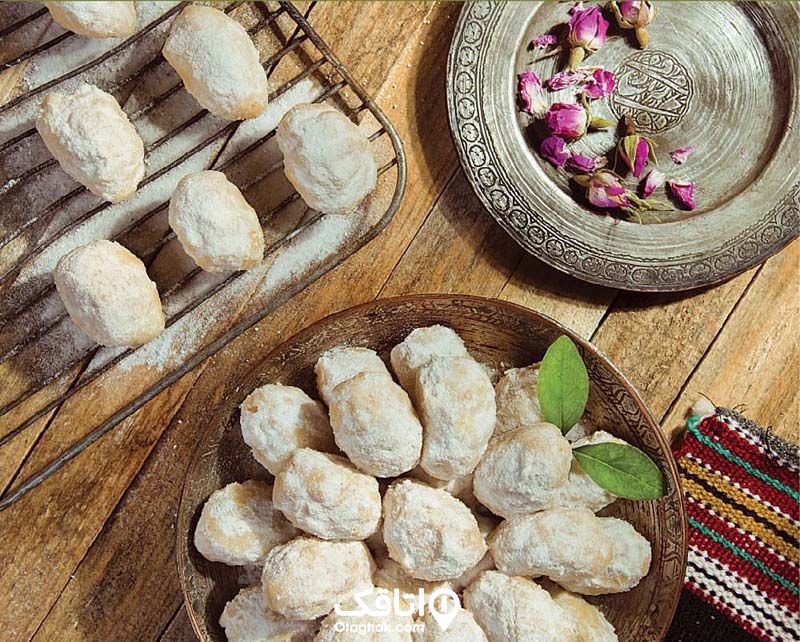شیرینی سرغبیلی در ظرف چوبی و مقداری گل سرخ در ظرفی فلزی