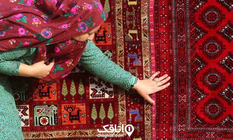 خانمی در حال لمس قالی قرمز با طرح ترکمن