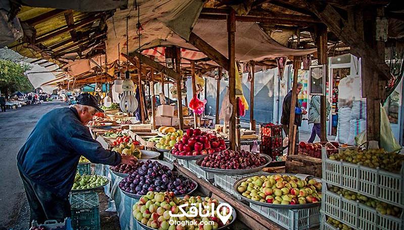 یازار روزی که در غرفه های آن انواع میوه از جمله سیب، زرد آلو، آلو و .. دیده می شود و مردی مسن در حال خرید میوه