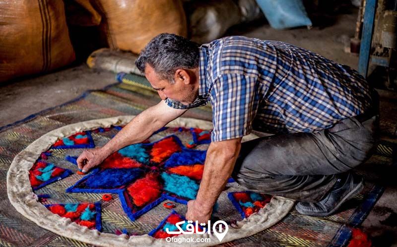 یک مرد خم شده روی یک رومیزی نمدی و در حال نمد بافی است