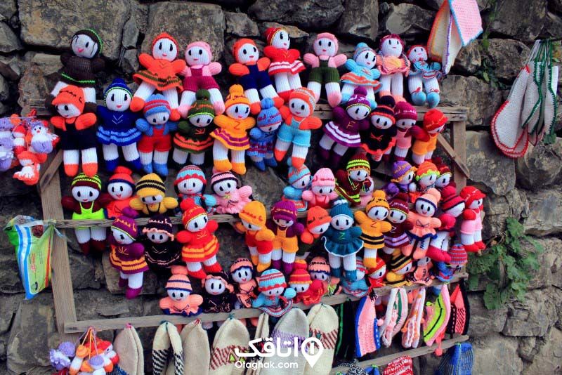 تعداد زیادی عروسک باقتنی با رنگ های متنوع سبز، قرمز، صورتی، بنفش ، سرمه ای و غیره که از یک چارچوب چوبی آویزان شده اند