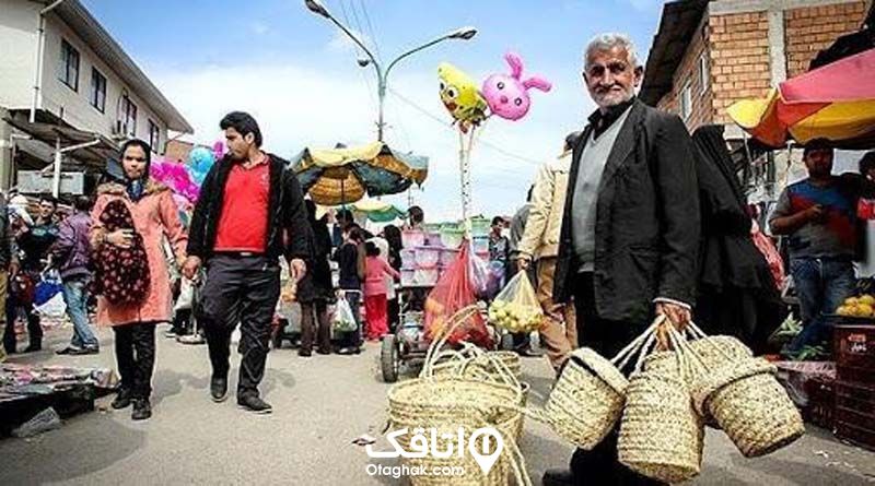 مردی مسن که چند سبد حصیری در دست دارد در میان بازار که مردم در حال خرید هستند