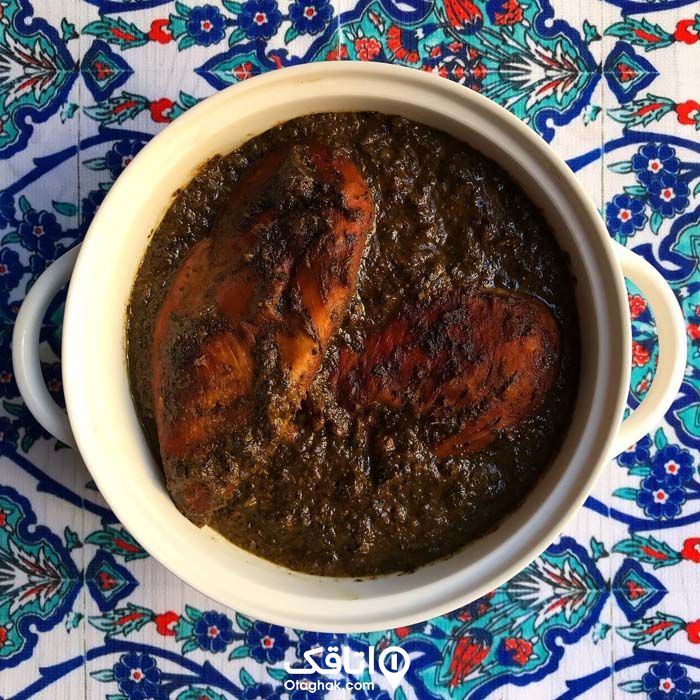 یک نوع غذای محلی با گوشت پرندگلن و سبزی محلی داخل قابلمه ای سفید رنگ بر روی سفره ای با طرح های سنتی آبی رنگ