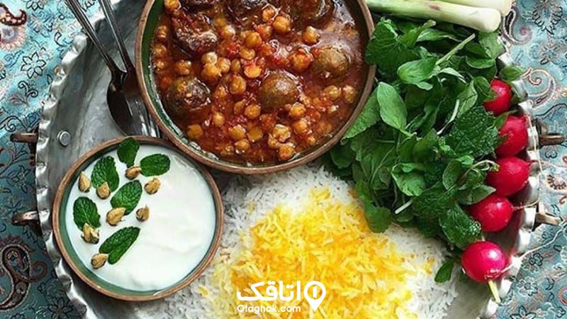 یک ظرف قیمه نخود، مقداری برنج، یک کاسه ماست تزیین شده با نعنای تازه و مقداری سبزی تازه در یک سینی فلزی کنگره دار بر روی سفره ای ترمه ای 