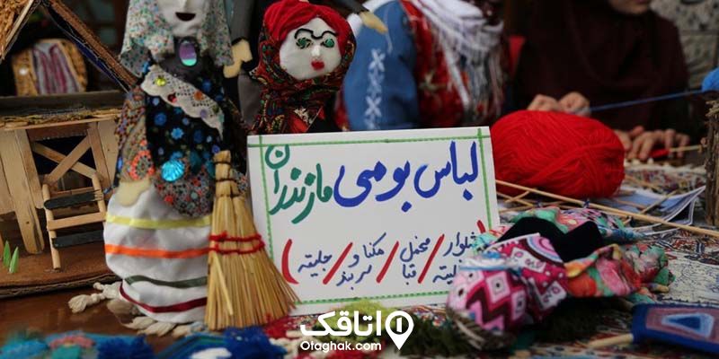 یک عروسک دست ساز با لباس محلی و یک نوشته که وسایل موجود در مغازه روی آن نوشته شده.