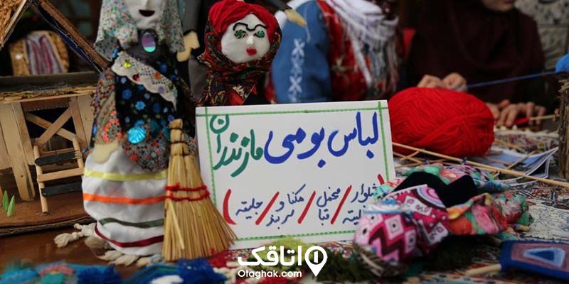 یک عروسک دست ساز با لباس محلی و یک نوشته که وسایل موجود در مغازه روی آن نوشته شده.