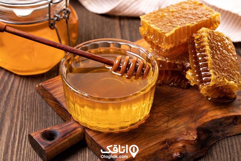 عسل طبیعی در یک کاسه روی یک تخته چوبی در کنار موم عسل