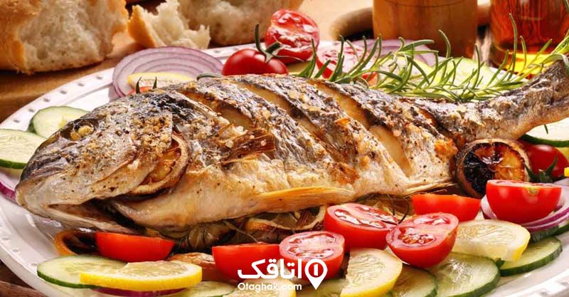 ماهی سرخ شده درون سینی با دورچین لیمو، گوجه، خیار و پیاز