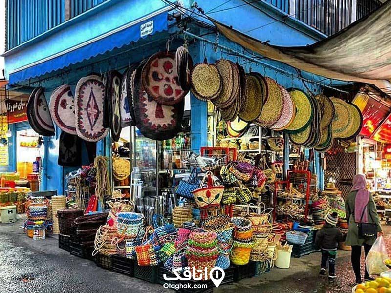 یک مغازه حصیر فروشی که تعداد زیادی سبد حصیری، انواع پادری و صنایع دستی دارد و در بازار محلی قرار دارد