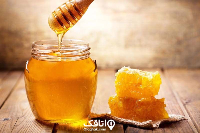 ظرف شیشه ای پر از عسل همراه با موم عسل در کنار آن
