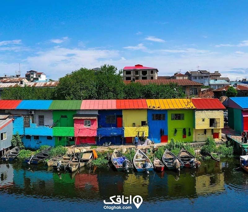 ساختمان های رنگی چسبیده بهم کنار رودخانه و قایق های پارک شده در ساحل رودخانه