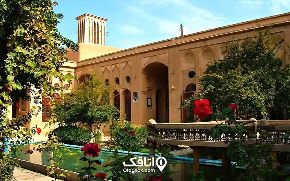 حوضی بزرگ، درختان سبز و گل های رنگارنگ و ساختمان قدیمی و زیبا با بادگیر بلند به نام عمارت لاری ها