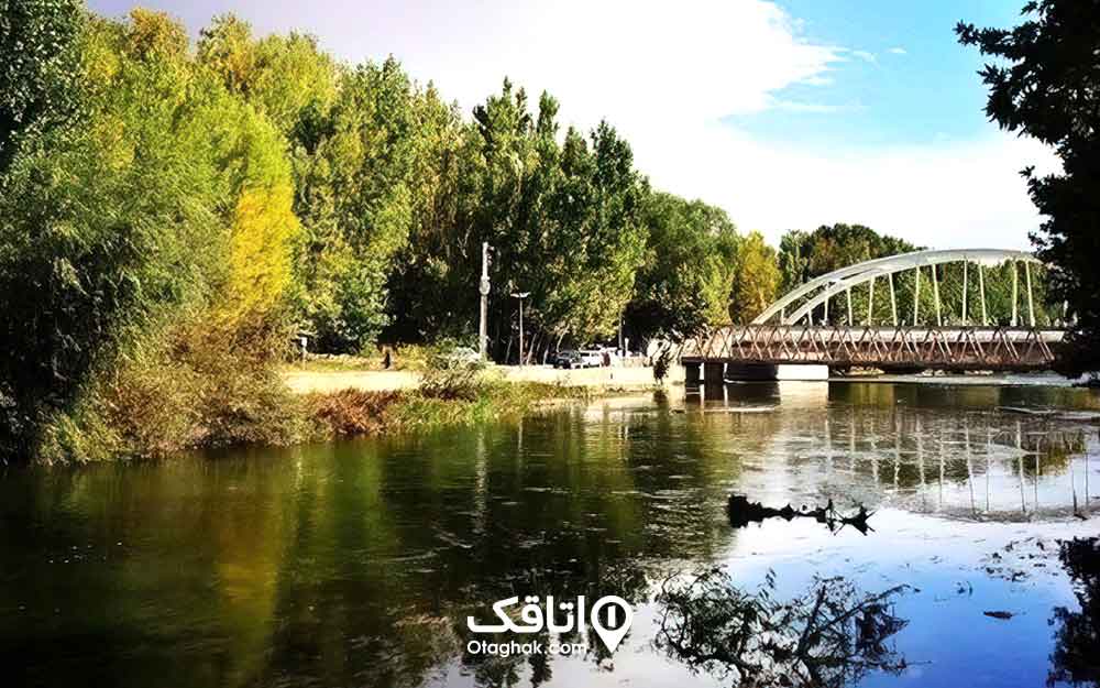 منطره ای با نمایی از یک پل بر روی رودخانه ای عرض و درختان انبود کنار رودخانه