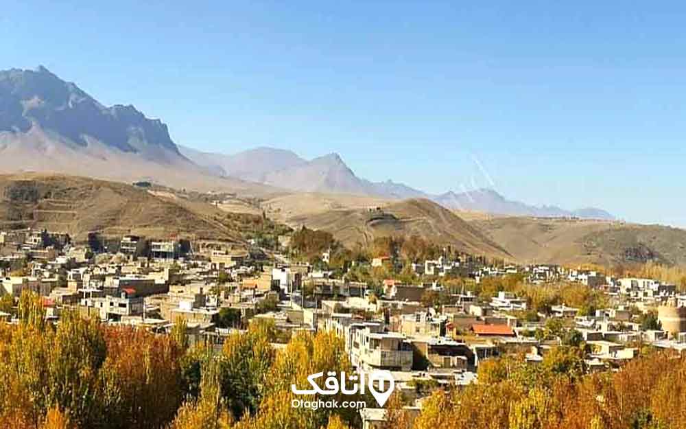 منظره ای از خانه ها، درختان، کوه ها و آسمان آبی یک روستا