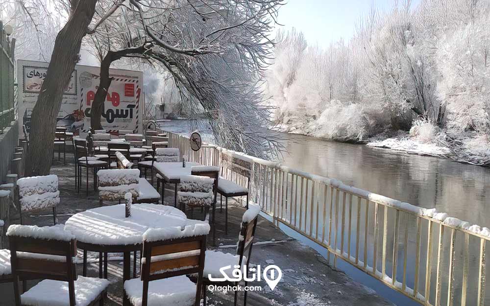 منظره برفی درختان و میز و صندلی های رستوران پوشیده شده از برف در کنار ودخانه