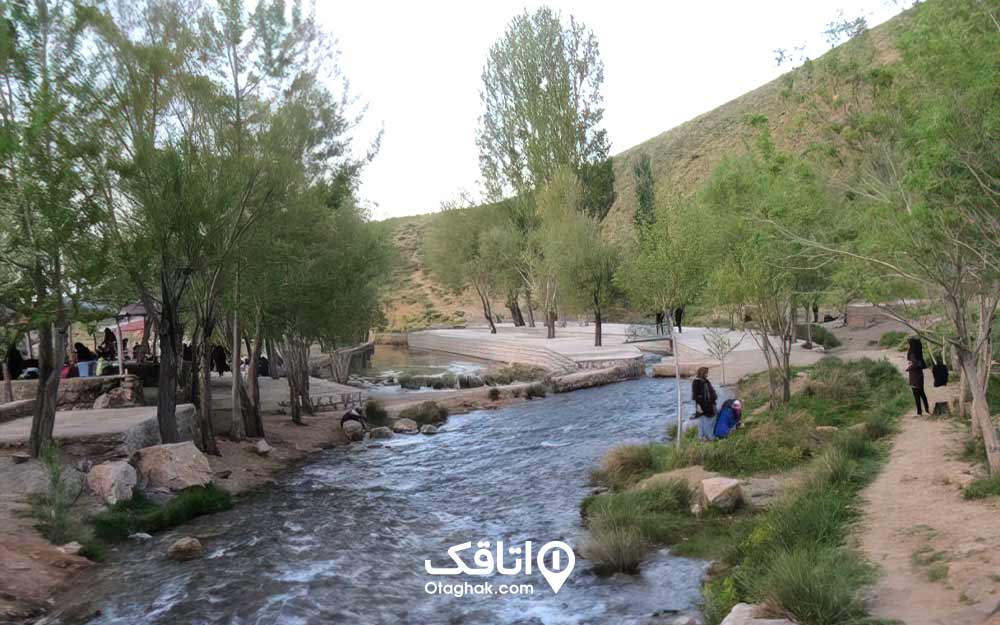 رودی بزرگ که اطراف آن کمی درخت و چمن است و افرادی در کنار آن نشسته در حال تفریح