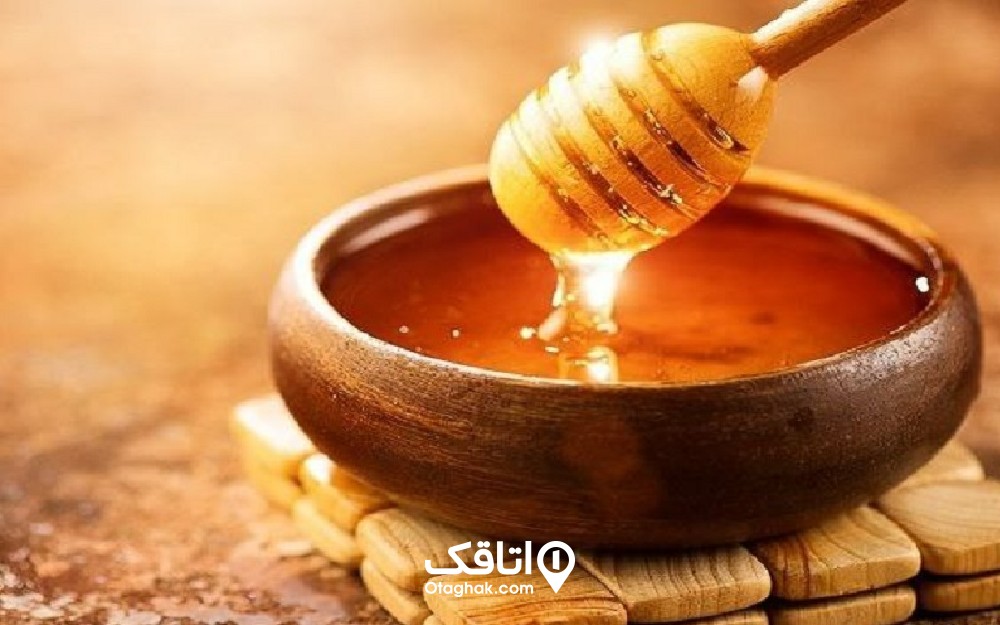 مقداری عسل در یک ظرف چوبی و یک عسل خوری چوبی