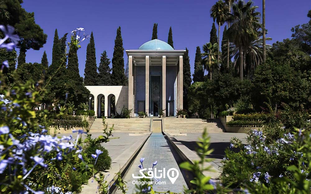 ساختمانی با گنبدی آبی رنگ و ستون هایی در جلو در میان باغی سر سبز و آرامگاه سعدی