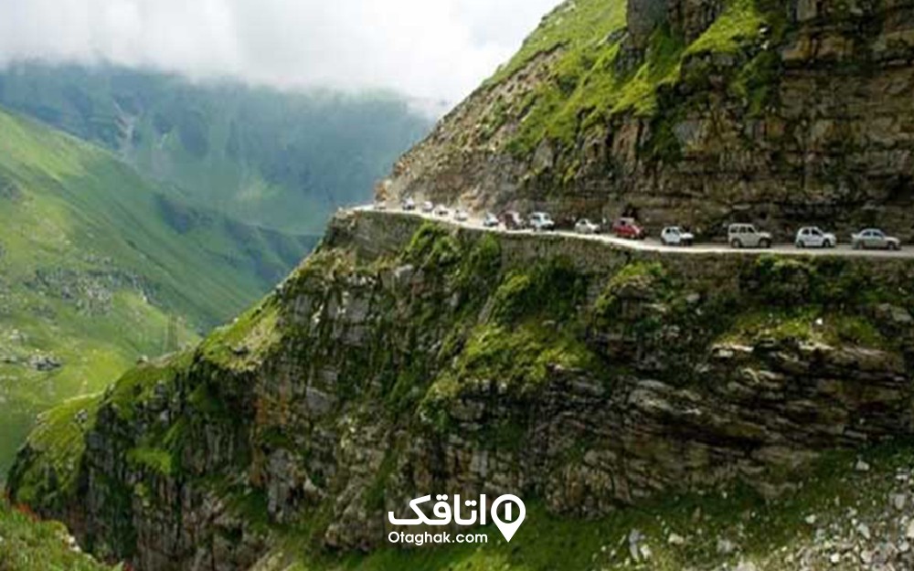 جاده ای در میان کوهستان سرسبز و وخودروهای که پشت هم در حال عبور از این جاده باریک هستند