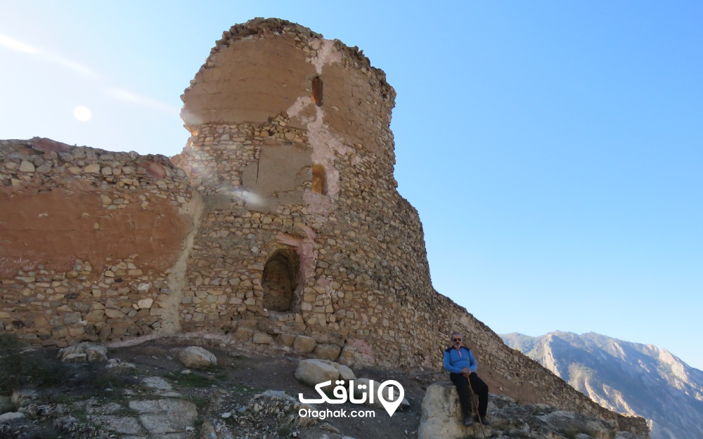 نمایی از کنار قلعه کنگلو و مردی که جلوی آن نشسته است