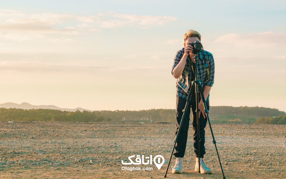 نمایی از عکاسی که با کمک دوربین و سه‌پایه عکاسی می‌کند.